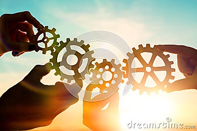 Four hands of businessmen collect gear from the gears of the details of puzzles. against the sunset. Stock Photo