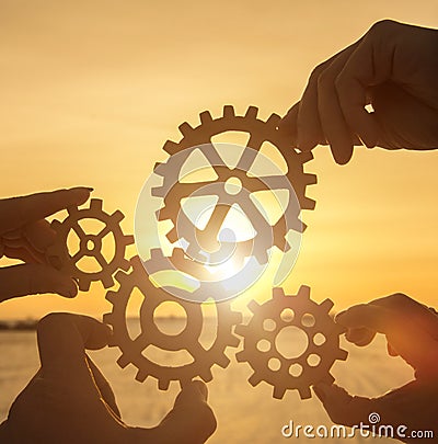 Four hands collect the gear from the gears of the details of the puzzles. Stock Photo