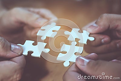 Four hands joining four white jigsaws together Stock Photo