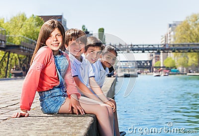 Four happy friends sitting in a line on embankment Stock Photo