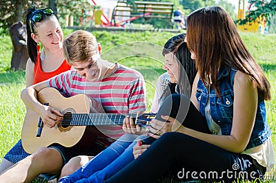 Four happy teen friends playing guitar in green summer park Stock Photo