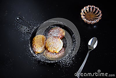 Four homemade fried pancakes in a small cast-iron frying pan. Rose jam. Black wood background. Stock Photo