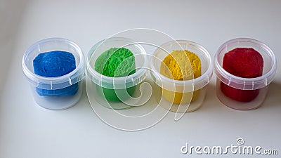 Four multi-colored plasticines in a container on a white table. Baby dough for modeling red blue yellow and green colors Stock Photo