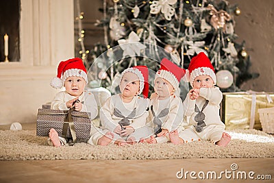 Four newborn kids in red Santa`s caps sitting on the floor in white Christmas studio Stock Photo