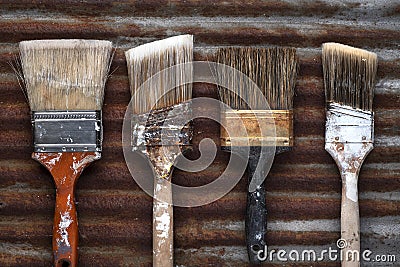 Four Old Crusty Household Paintbrushes on Rusted Corrugated Metal Background Stock Photo