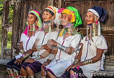 Four Padaung women in traditional dress and with metal rings around their neck are sitting next to each other in the village Editorial Stock Photo