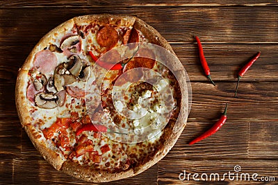 Four-part assorted pizza and red chilli peppers on natural pine plank wood surface. Food for gourmets Stock Photo