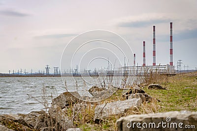 Four pipes of a power plant on the shore of a reservoir in a spring cloudy day, against a blue sky with clouds. Stock Photo