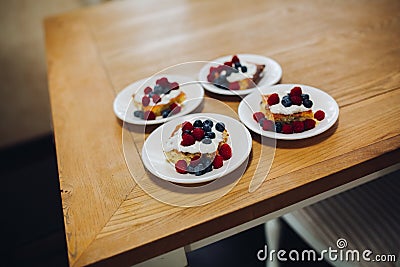Four portion of sweet bake with raspberry, blueberry and cream on wooden table. Stock Photo