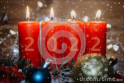 Four red Advent candles with 2022 figures on them and Christmas decorations lying in the snow as a template Stock Photo