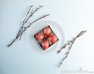 Four red Easter eggs in square cardboard box with willow branches on pale blue background. Stock Photo