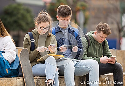 Four teenagers enthusiastically look at the screens of their smartphones on street Stock Photo