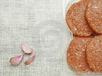 Four uncooked raw turkey burgers with red barbeque flavoring in a plastic packaging on a white simple table cloth and three garlic Stock Photo