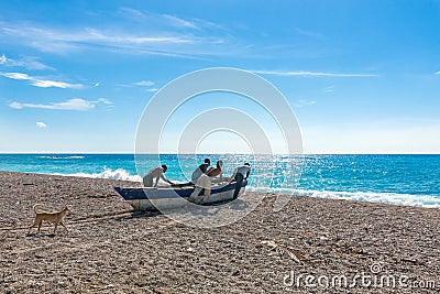 Four unidentified local fishermen pushing their boat to the sea and preparing for fishing, dog following them Editorial Stock Photo