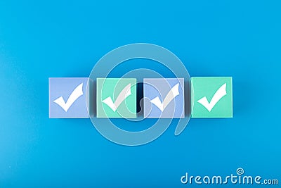Four white checkmarks on multicolored cubes in a row against blue background Stock Photo