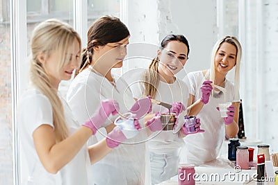 Four women mixing pants for creating abstract picture in white modern loft studio interior with big windows. Teamwork Stock Photo