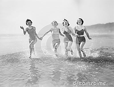 Four women running in water on the beach Stock Photo