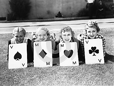 Four women are well suited to lay on the grass with playing cards in front of them Stock Photo