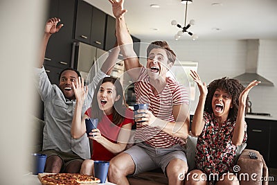 Four young adult friends watching sports on TV celebrating Stock Photo