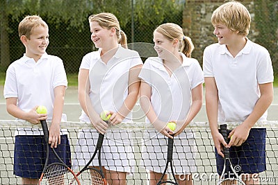 Four young friends on tennis court smiling Stock Photo