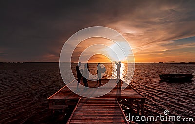 Four young guys and girls taking a picture of the sunset on the water with a smart phone, from a wood pier Editorial Stock Photo
