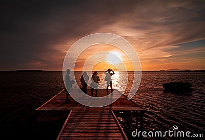 Four young guys and girls taking a picture of the sunset on the water with a smart phone, from a wood pier Editorial Stock Photo