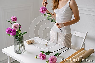 Fragile female florist collects bouquet of pink dahlias in a vase at white table. An image for your floral design Stock Photo