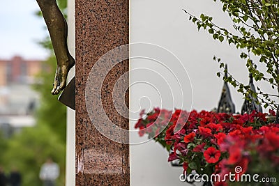 Fragment of crucifix. Bronze statue of crucifixion of Jesus Christ. Red flowers near the crucifix. Stock Photo