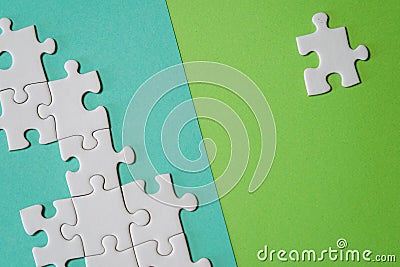 Fragment of a folded white jigsaw puzzle and a pile of uncombed puzzle elements against the background of a colored surface Stock Photo