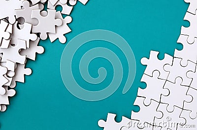 Fragment of a folded white jigsaw puzzle and a pile of uncombed puzzle elements against the background of a blue surface. Texture Stock Photo