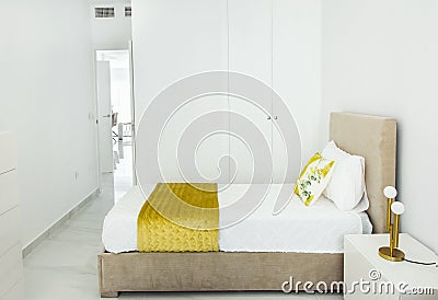 Fragment of modern bedroom in minimalist white and yellow interior design style with built-in closet. Bed with pillows duvet Stock Photo