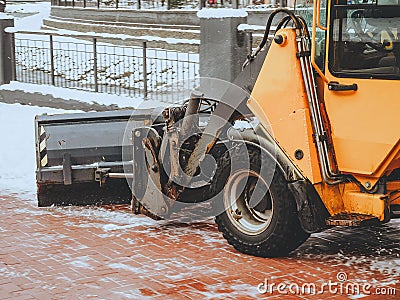 Fragment of orange bulldozer raking snow from tiles Stock Photo