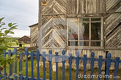 A fragment of a wooden house with an old blue fence in the village in the evening Stock Photo