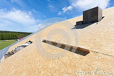 Frame house under construction. Roof with installed fiber board and plastic mansard or skylight window. Stock Photo