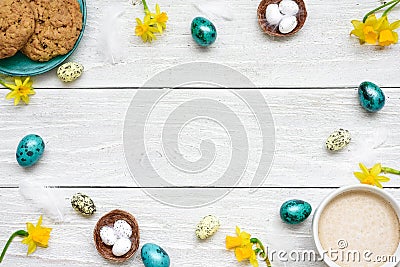 Frame made of easter eggs, cup of cappuccino, spring flowers and biscuits on white wooden background. easter composition Stock Photo