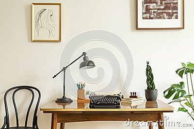 Framed drawing on a white wall above an antique, wooden desk with a vintage, black typewriter in a home office interior Stock Photo