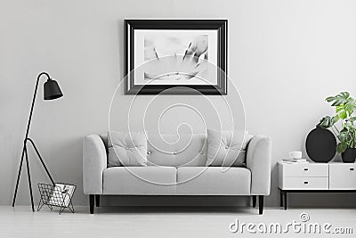 Framed photo on a wall above a fancy, gray sofa with cushions in a minimalist living room interior and place for a table. Real pho Stock Photo