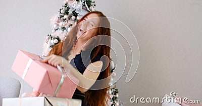 Frau mit langen roten Haaren, die sich mit Geschenken in der Nähe eines verzierten Weihnachtsbaumes amüsiert stock video footage Frau mit langen roten Haaren, die sich mit Geschenken in der Nähe eines verzierten Weihnachtsbaumes amüsiert stock video footage