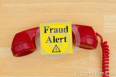 Fraud alert on sticky note with a retro red phone on textured wood desk Stock Photo