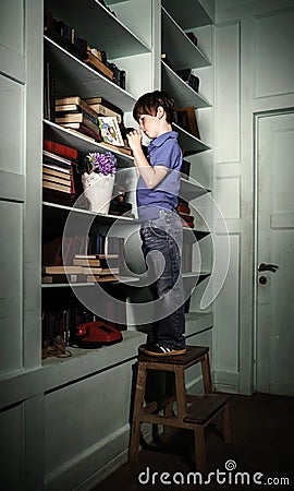 Freckled red-haired little boy searching book on bookcase Stock Photo