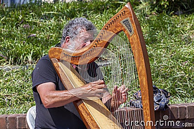 Closeup image of a street musician performing on the sidewalk by playing his harp. Editorial Stock Photo