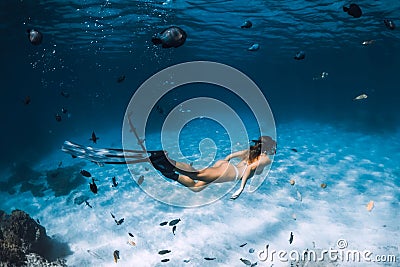 Free diver woman with fins glides over sandy bottom with fishes in transparent sea Stock Photo