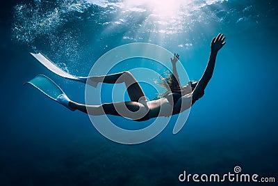 Free diver woman with white fins glides underwater with amazing sun rays. Freediving underwater in sea Stock Photo