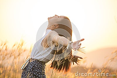 Free happy woman enjoying sunset. Beautiful woman in white dress embracing the golden sunshine glow of sunset with arms outspread Stock Photo