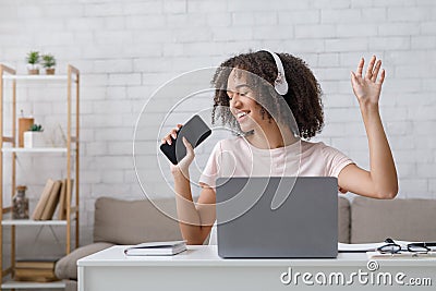 Free time after online lectures. Cheerful african american girl in headphones singing in smartphone Stock Photo