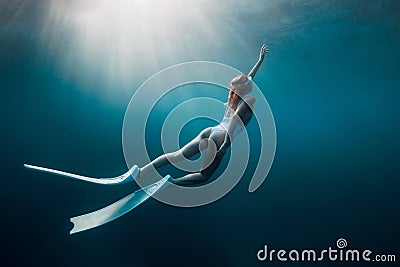 Freediver woman with white fins underwater. Freediving with beautiful girl in ocean and sun rays Stock Photo