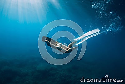 Freediver young woman with white fins glides undersea with sun rays. Freediving in transparent sea Stock Photo