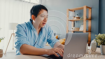 Freelance Asia guy casual wear using laptop online in living room at home office. Working from house, remotely work, distance Stock Photo