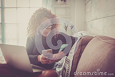 Freelance people at work at home - beautiful adult caucasian woman sit on the sofa with phone device and laptop computer working - Stock Photo