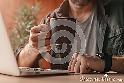 Freelancer drinking coffee and working at home office on laptop computer Stock Photo